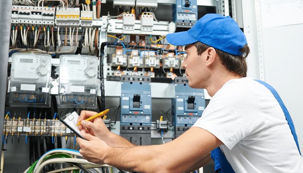 électricien qui regarde un tableau électrique et qui prend des notes